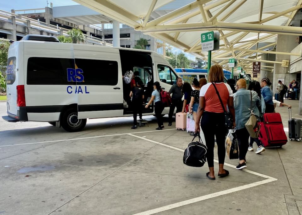 Passengers line up to board an off-airport shuttle at parking spot B12.
