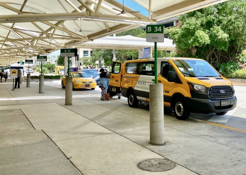 A taxi van is parked in spot B34 while a passenger loads their luggage.