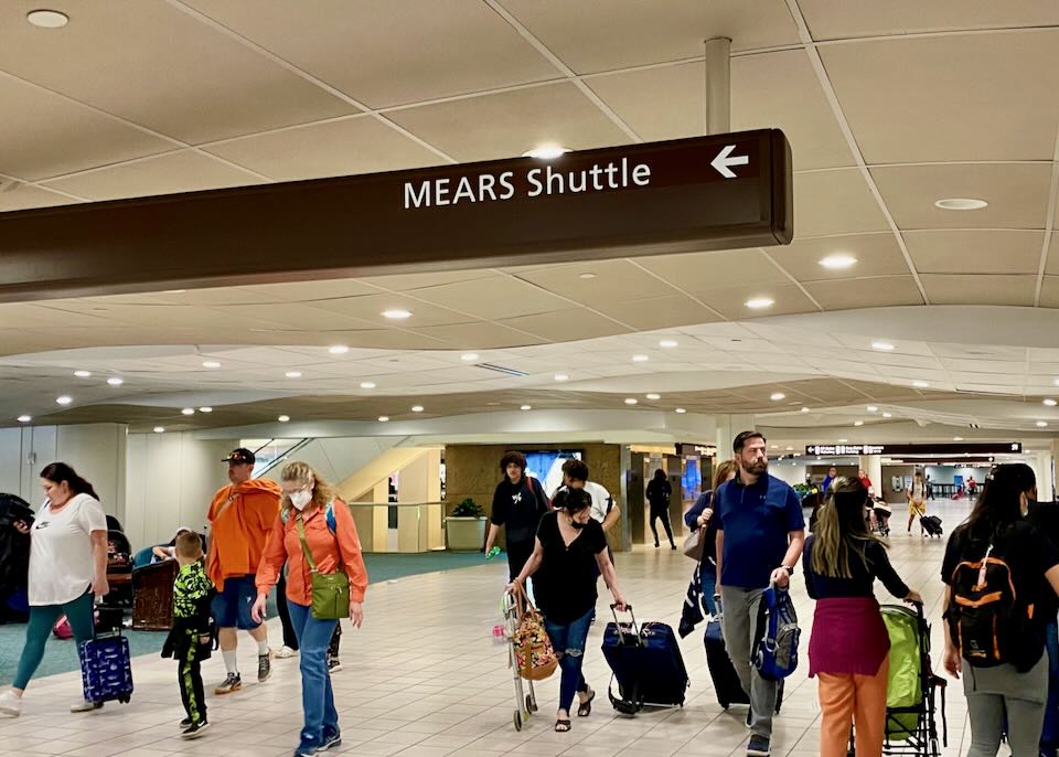 Inside the airport, an overhead sign reads, MEARS shuttle.