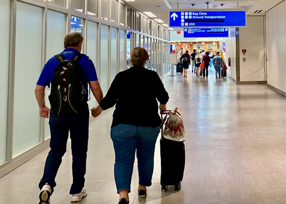 A couple hold hands walking toward baggage claim.