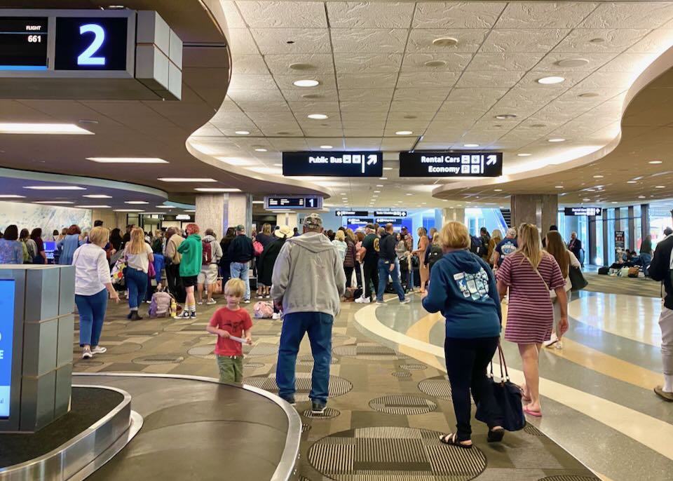 People stand around a luggage carousel, waiting for their luggage.
