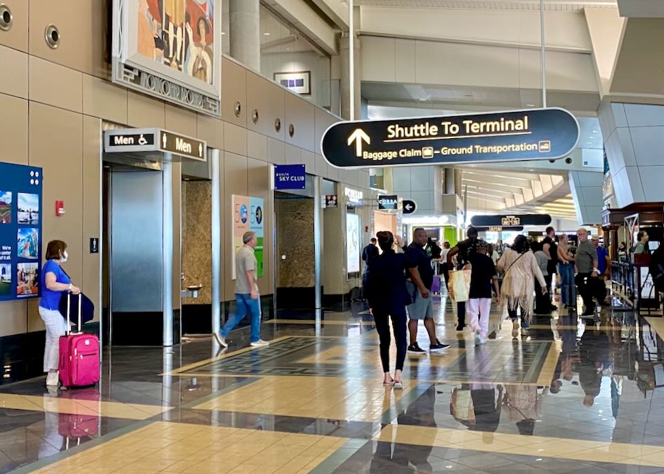 Passengers walk under an airport sign pointing to the "Shuttle to Terminal."