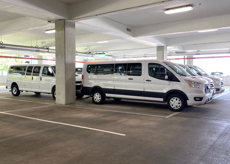 Several white passenger vans sit parked in the Enterprise area of the garage.