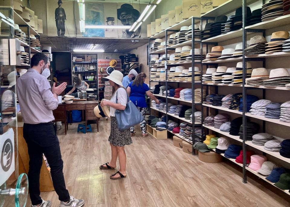 A man helps a customer select a hat from many on a shelf