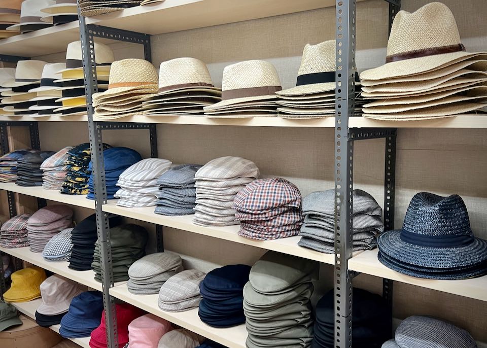 Piles of cloth newsboy caps and straw fedoras displayed on a shelf.