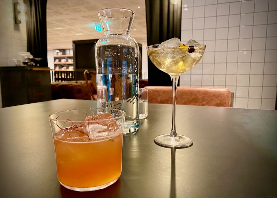 Two beautiful cocktails resting on a table next to a carafe of water