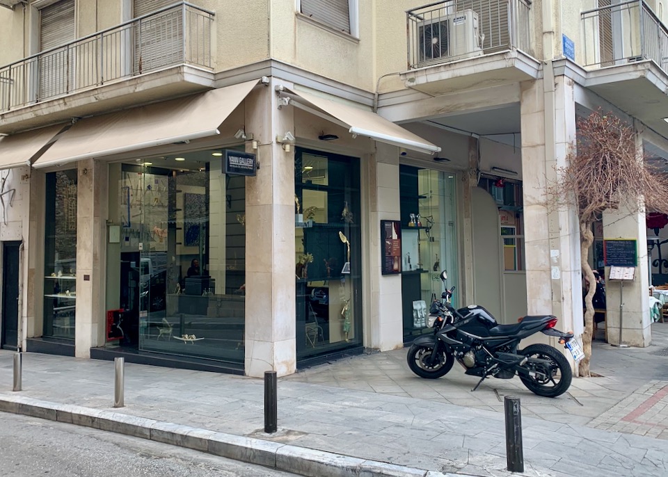 Exterior of a sculpture gallery on an urban streetcorner with a motorcycle parked in front.