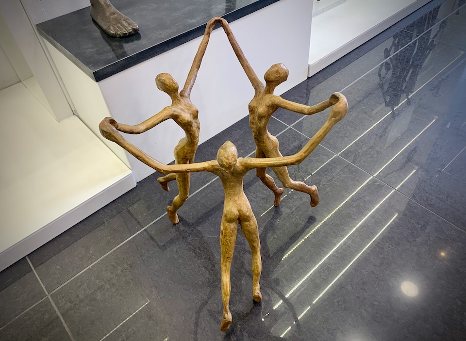 Bronze sculpture of three women holding hands and dancing