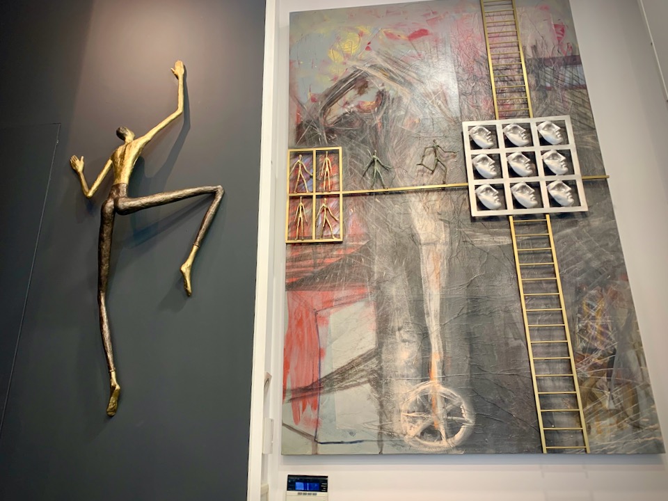 A metal sculpture of a man climbing a wall, displayed next to a colorful mixed-media painting