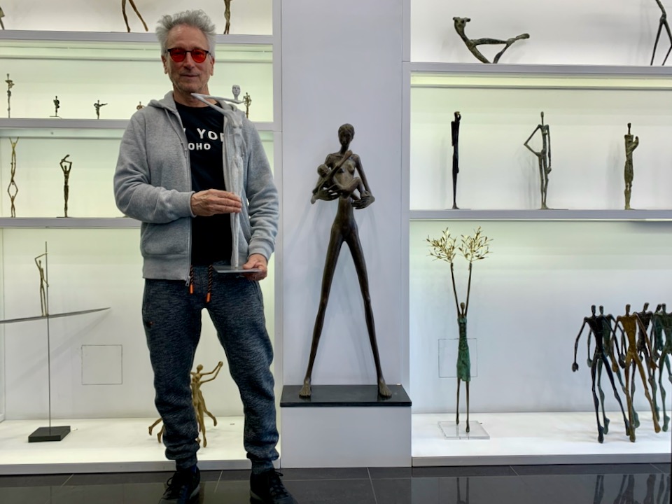 A hip, gray-haired artist presemts a piece of his metal sculpture to the camera 