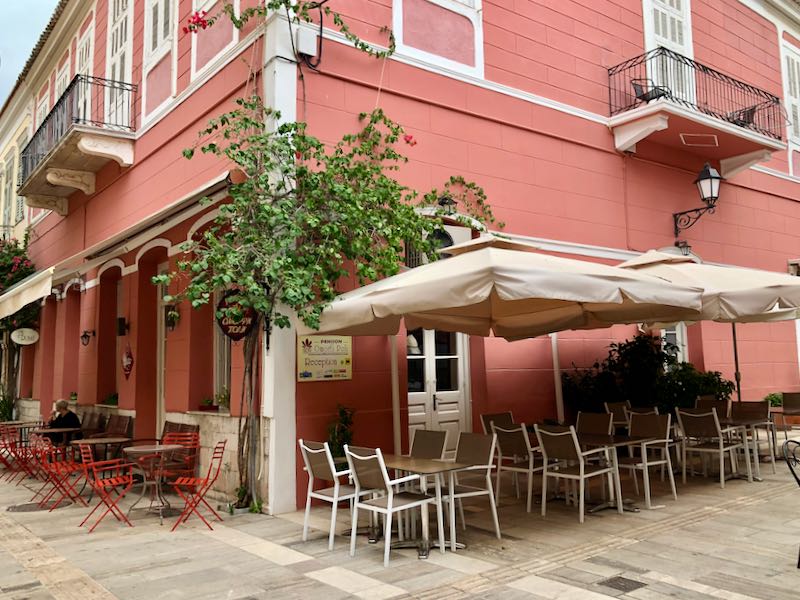 Exterior of a charming pink hotel with cafe tables and potted plants in front