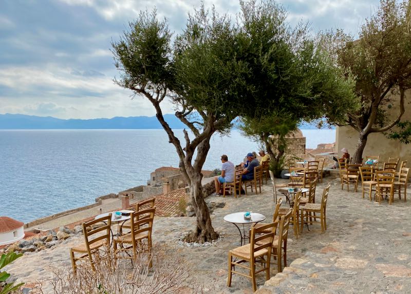 Wooden chairs and cafe tables on a stone terrace overlooking the sea