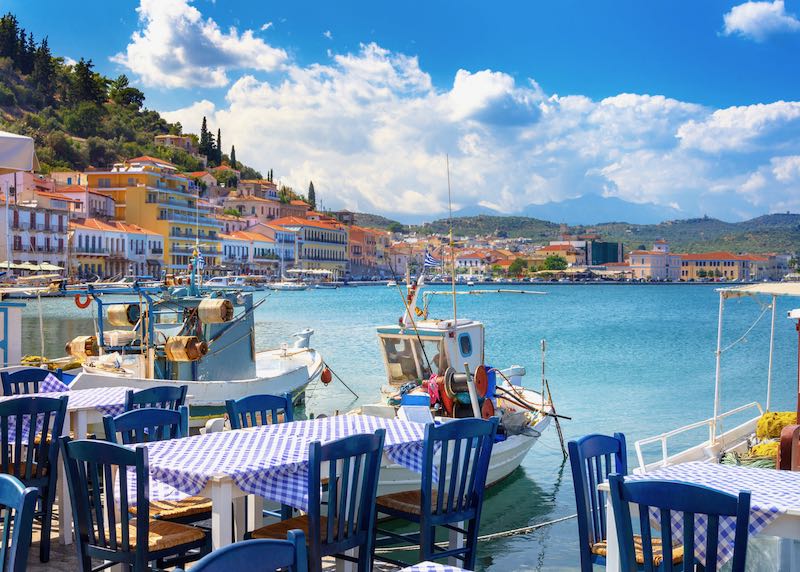 View over colorfully-dressed tables of a waterfront taverna to the blue sea.