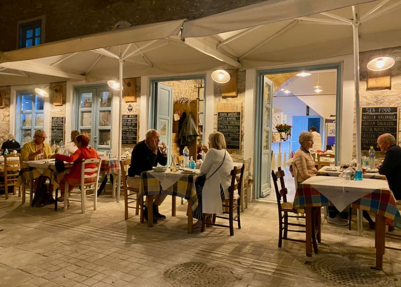 Diners at outdoor tables of a rustic Greek taverna at night