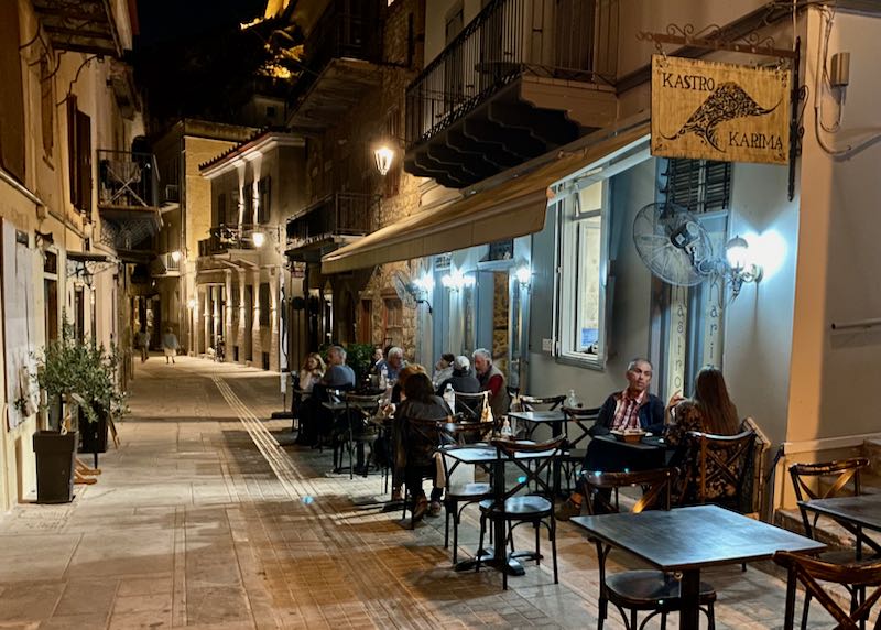 Diners sit at outdoor tables at a rustic café in a marble pedestrian alley at night