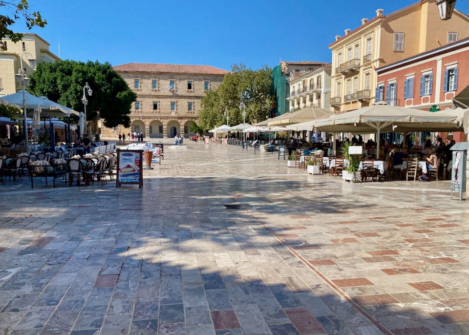 Marble-paved village square surrounded by Venetian-style and Neoclassical buildings and cafes.