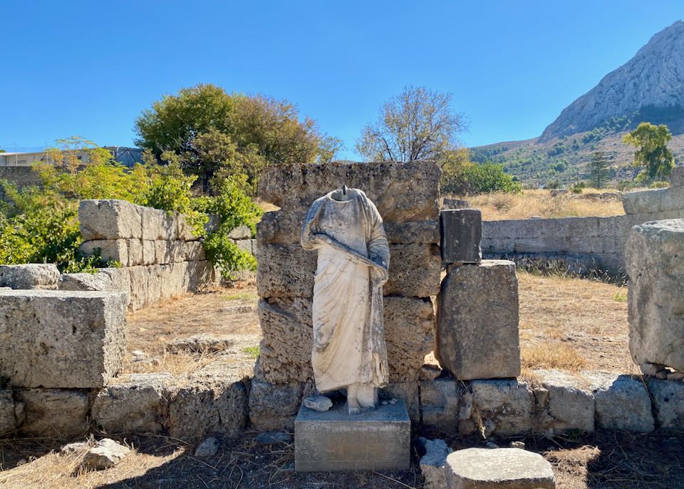 Roman statue of a woman in a gown (missing a head) in front of the stone ruins of a building.