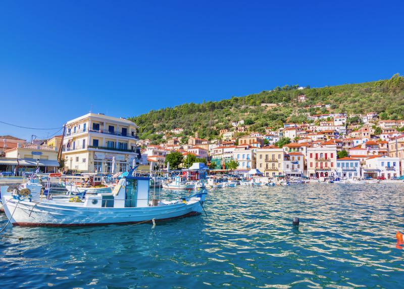 Blue-water harbor lined with colorful Greek buildings and boats