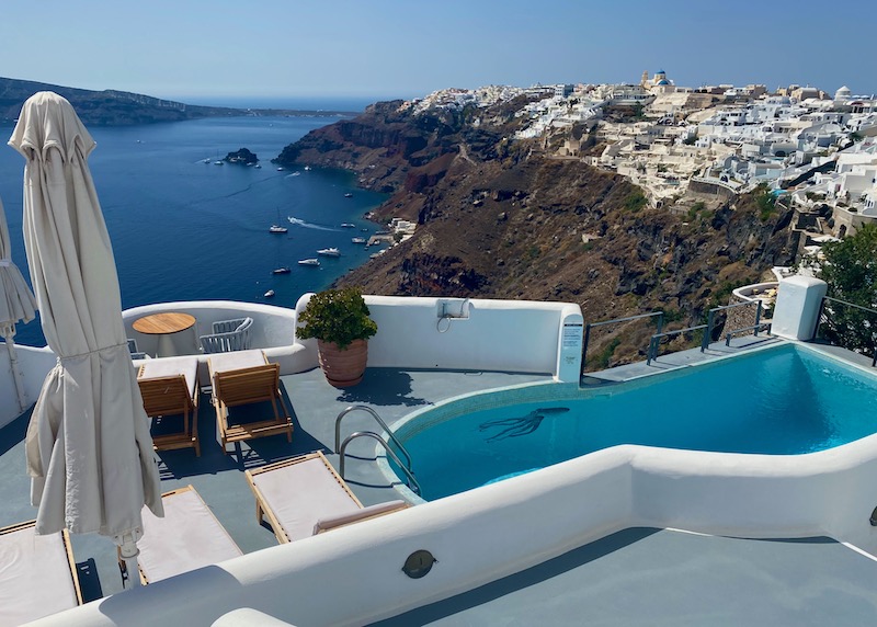 Pool and sun terrace with a view of Oia village and the caldera at Ikies in Santorini