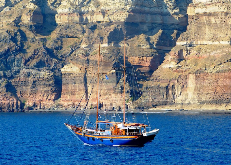 Sailboat in the caldera with colorful cliffs and a black beach.