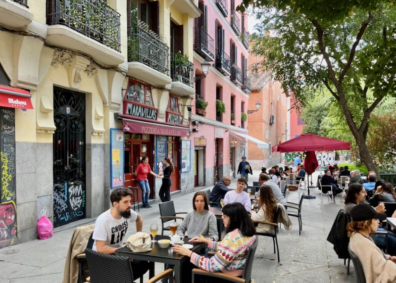 People eat at outdoor tables sidewalks lined with colorful buildings