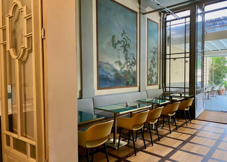 Small dining tables lining a wall of hand-painted murals of flora and fauna