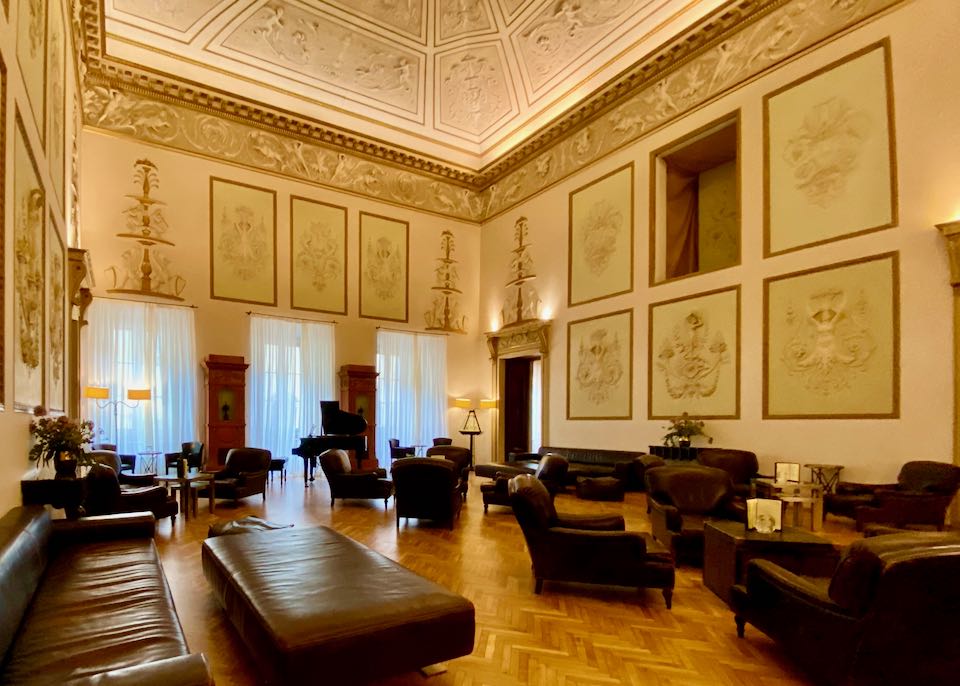 Large room with towering ceilings, a grand piano, and many leather chairs and sofas
