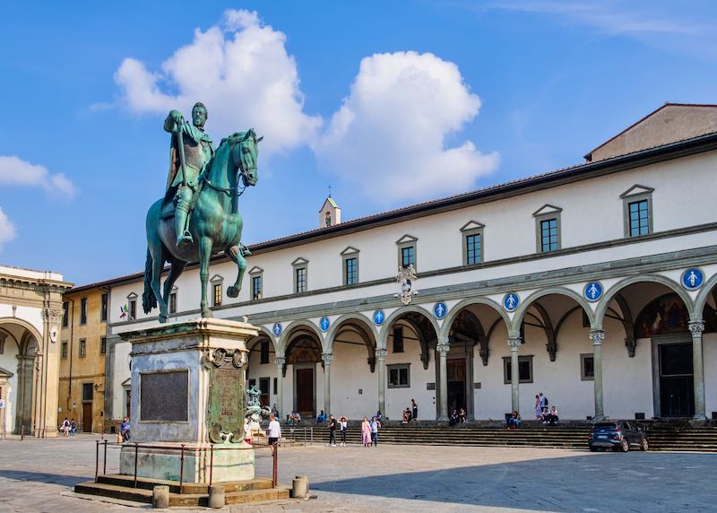 Square lined with an arched colonnade, with a statue of a man on a horse at its center
