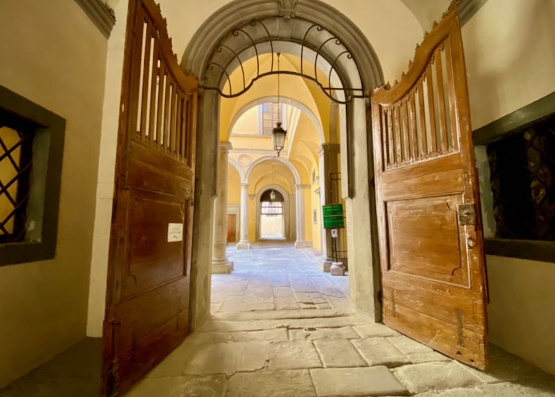 Large antique wooden doors open to a bright yellow palazzo entrance 