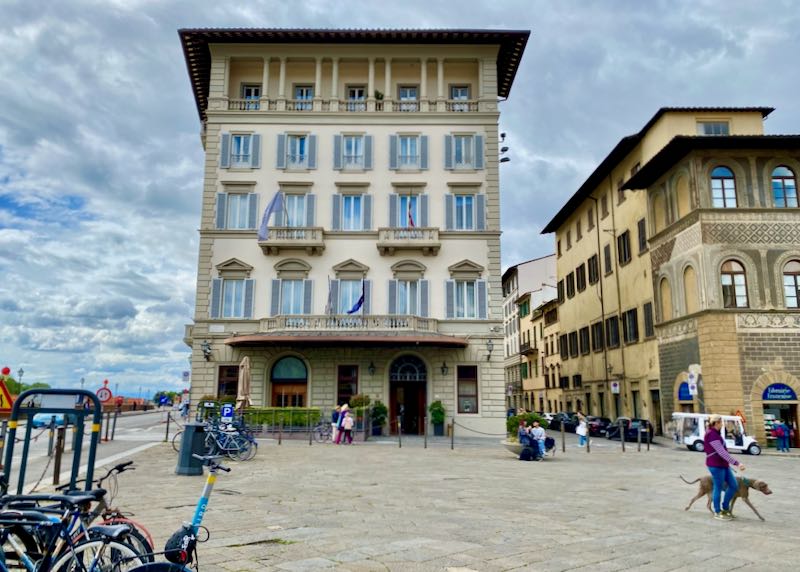 Exterior of a Florentine-style hotel in a cobblestone square, with pedestrians passing by