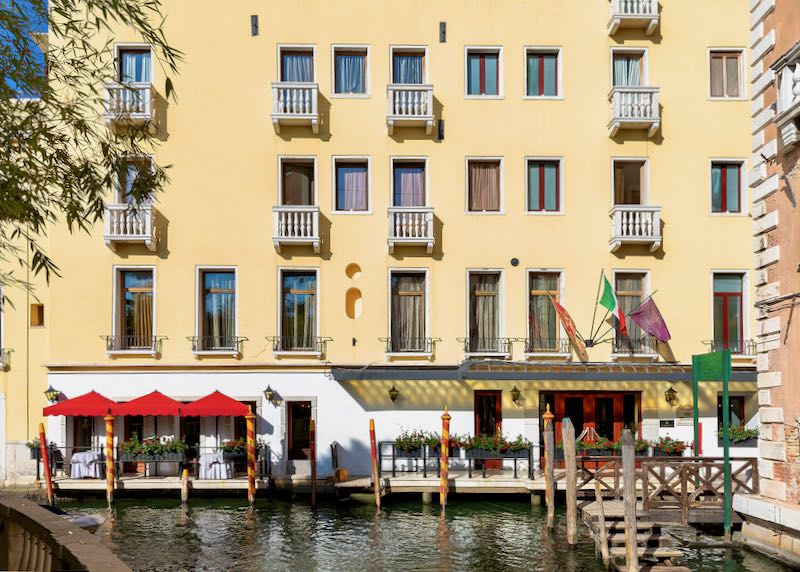 Yellow exterior of a hotel on a Venetian canal on a sunny day