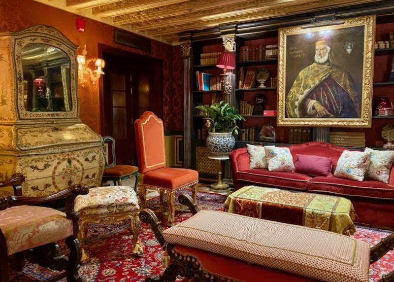 Plush and ornate living room with velvet furnishings in dark reds and oranges and a large oil painting of a Venetian doge