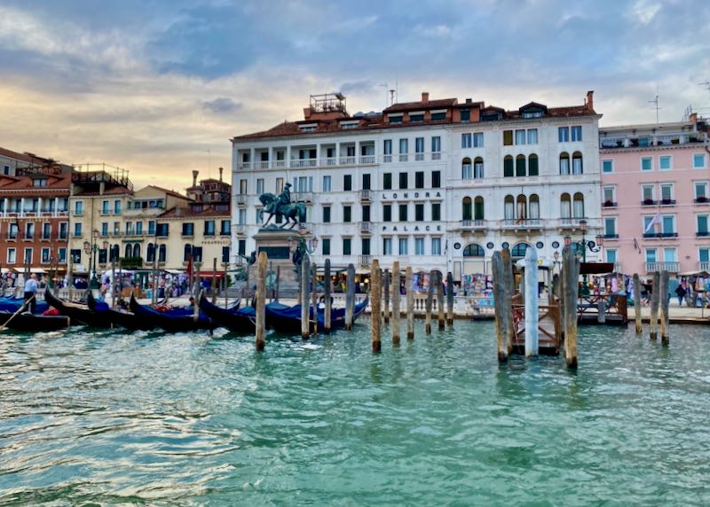 A large luxury hotel on Venice's Grand Canal with gondolas in front, at dusk