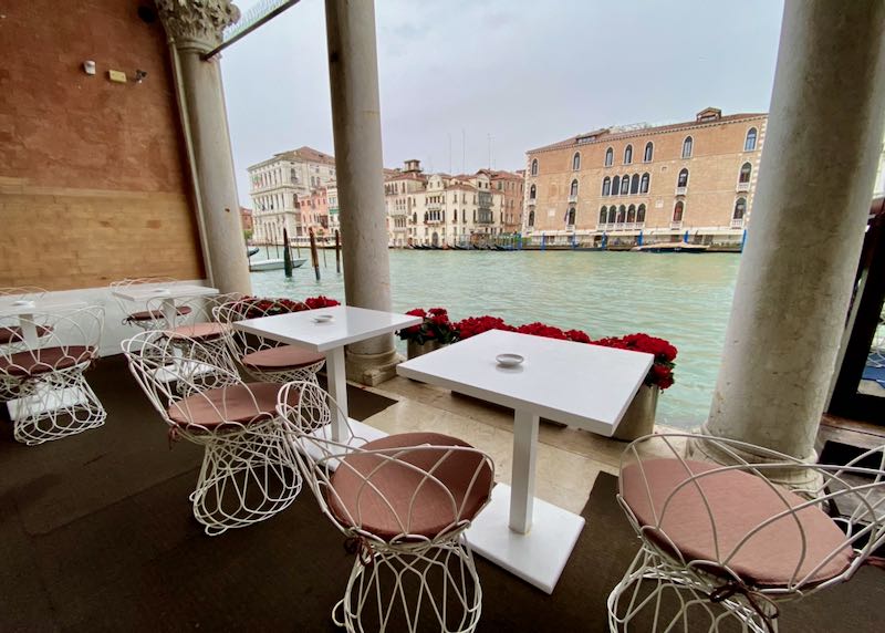 View of Venice's Grand Canal from a terrace set with small cafe tables
