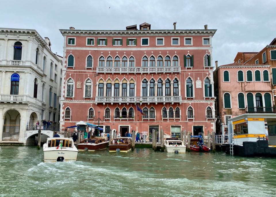 A beautiful pink venetian hotel on the Grand Canal with a boat pulling up to the dock