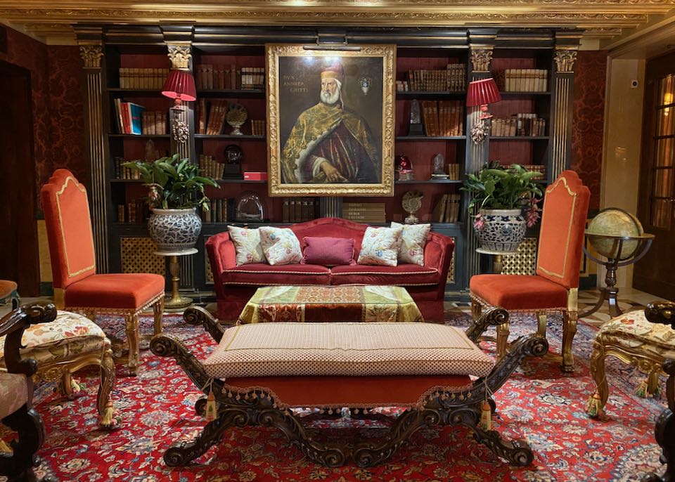 A plush room lined with bookshelves and featuring a large oil painting of a Venetian doge