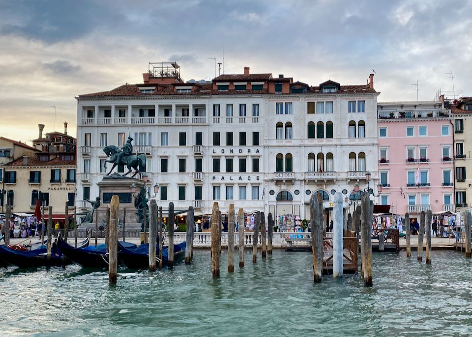 waterfront view of an Elegant Venetian building with docks and gondolas in the foreground.