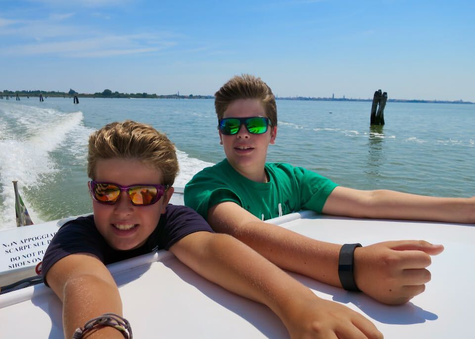 Two young, smiling boys in a boat on the Venetian lagoon.