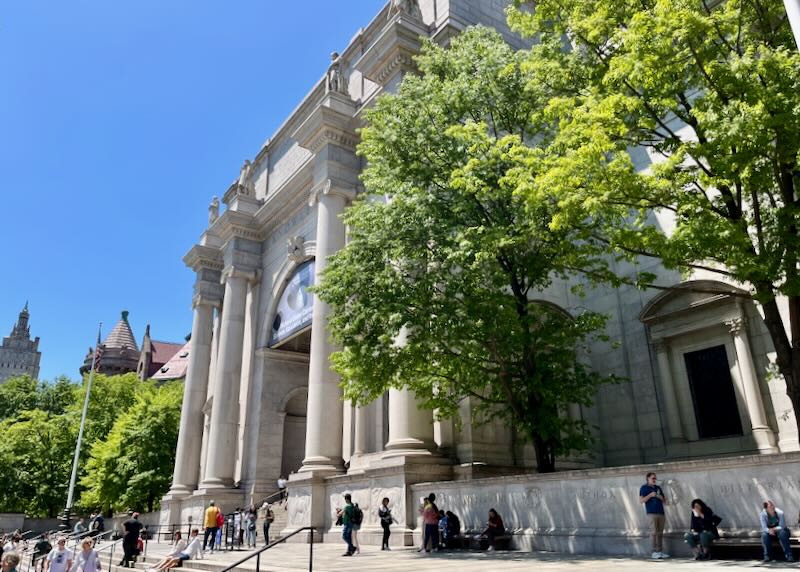 People sit on the steps in front of the Museum of Natural History in New York