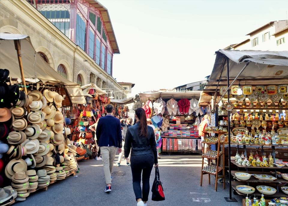 Shoppers walk through an outdoor marketplace selling hats and colorful trinkets