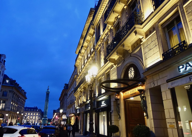 Haussmann-style exterior of the Park Hyatt Vendome in Paris with a pale stone facade, black wrought iron balconies, and statuettes on either side of the entrance.