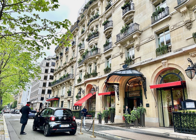 Opulent Haussmann-style facade with iron balconies and trailing vines, an iron-and-glass portico, and red awnings at the Plaza Athenee in Paris