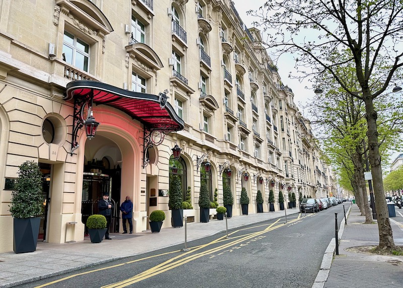 Exterior of Raffles Royal Monceau with a doorman and valet standing under a red glass awning in Paris