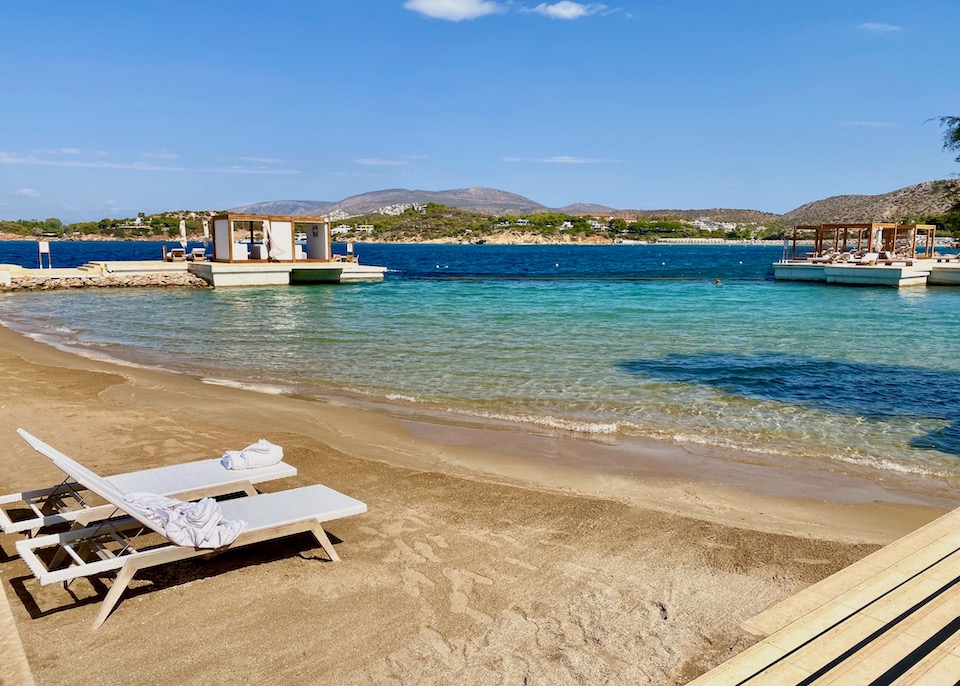 Two sunbeds on a quiet beach with cabanas in the background in Vouliagmeni on the Athens Riviera