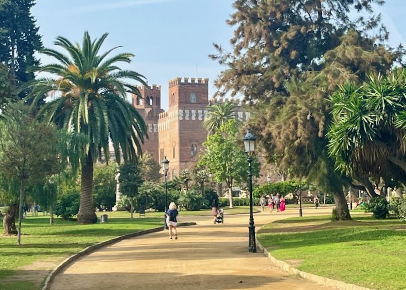 People walk up a gravel palm-lined path to a medeival looking castle
