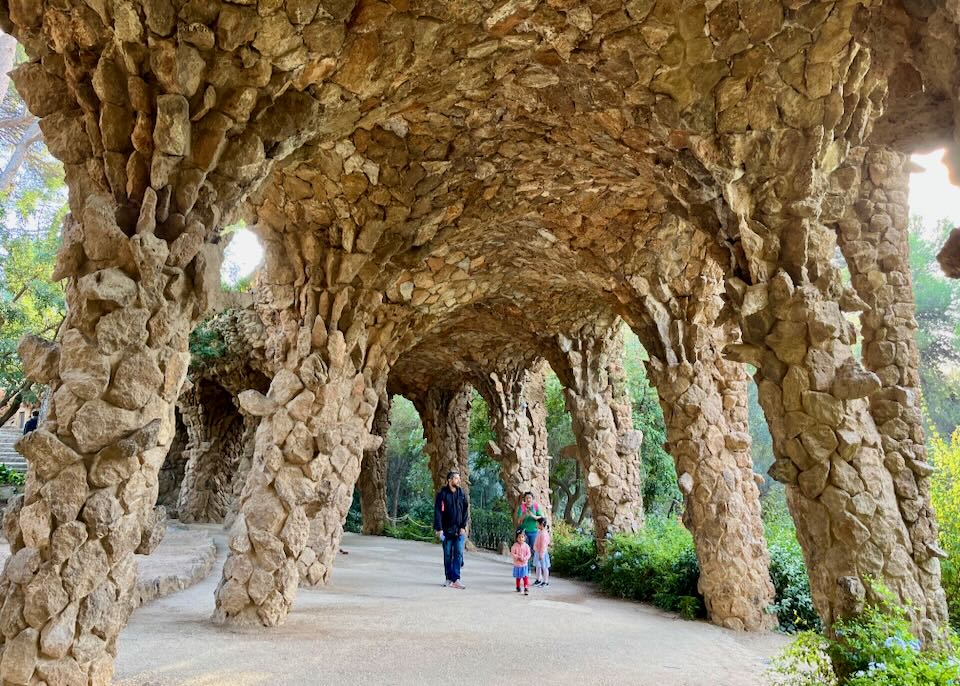 A man and two small children walk underneath modernist cave-like arches in a park setting.