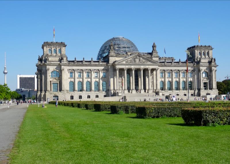 The glass-domed Reichstag Building on a green lawn on a sunny day