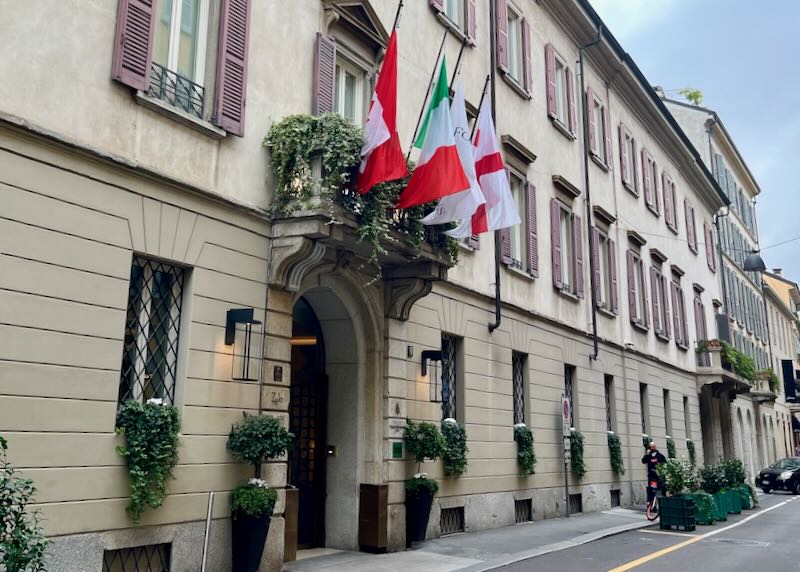 Exterior hotel entrance with topiary olive trees and Italian flags above the door