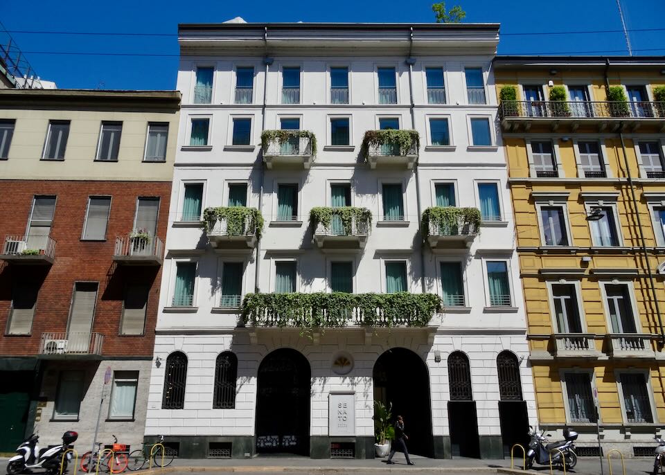 Exterior of a white Italianate hotel with arched doorways and plant-filled balconies