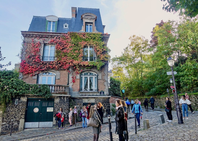 Red, orange, and green ivy leaves climbing a historic home on a curvy hilltop street in Montmartre, Paris